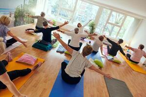 A group of senior women engage in various yoga exercises, including neck, back, and leg stretches, under the guidance of a trainer in a sunlit space, promoting well-being and harmony photo