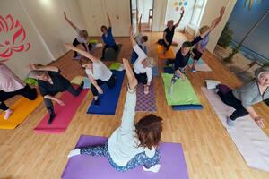 A group of senior women engage in various yoga exercises, including neck, back, and leg stretches, under the guidance of a trainer in a sunlit space, promoting well-being and harmony photo