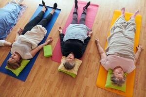 Top view of group of senior women engage in various yoga exercises, including neck, back, and leg stretches, under the guidance of a trainer in a sunlit space, promoting well-being and harmony photo