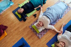 Top view of group of senior women engage in various yoga exercises, including neck, back, and leg stretches, under the guidance of a trainer in a sunlit space, promoting well-being and harmony photo