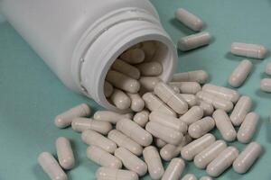bottle of pills, some of which spilled onto a light blue surface photo