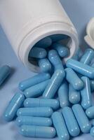 bottle of pills, some of which spilled onto a light blue surface photo