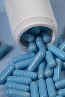 bottle of pills, some of which spilled onto a light blue surface photo