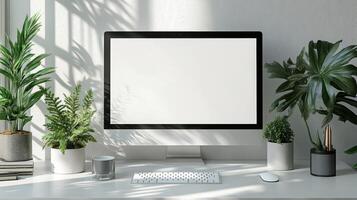 A modern desktop setup featuring blank computer screen surrounded by lush green plants, creating serene and inviting workspace. photo