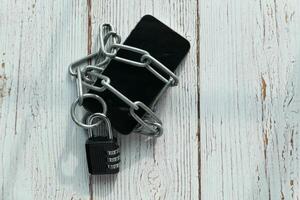 A mobile phone is securely locked with chains on a wooden surface, showing its protection photo