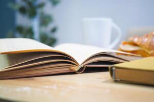 An open book with its pages gently turning rests on a wooden table in the breeze photo