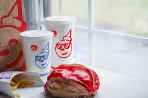 WASHINGTON, USA - August 08, 2024 - A table setting featuring a fast food order from Jack in the Box. The meal includes two white styrofoam cups with red lids and straws, and a wrapped burger. photo