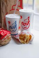 WASHINGTON, USA - August 08, 2024 - A classic fast food spread from Jack in the Box two cups of soda, a bag of fries and a wrapped burger. The cups feature the chain's iconic mascot with sunglasses. photo