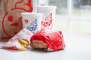 WASHINGTON, USA - August 08, 2024 - A classic fast food spread from Jack in the Box two cups of soda, a bag of fries and a wrapped burger. The cups feature the chain's iconic mascot with sunglasses. photo