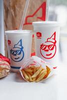 WASHINGTON, USA - August 08, 2024 - A classic fast food spread from Jack in the Box two cups of soda, a bag of fries and a wrapped burger. The cups feature the chain's iconic mascot with sunglasses. photo