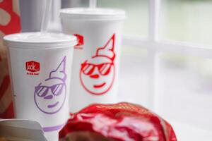WASHINGTON, USA - August 08, 2024 - A table setting featuring a fast food order from Jack in the Box. The meal includes two white styrofoam cups with red lids and straws, and a wrapped burger. photo