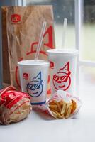 WASHINGTON, USA - August 08, 2024 - A classic fast food spread from Jack in the Box two cups of soda, a bag of fries and a wrapped burger. The cups feature the chain's iconic mascot with sunglasses. photo