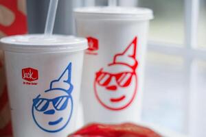 WASHINGTON, USA - August 08, 2024 - A table setting featuring a fast food order from Jack in the Box. The meal includes two white styrofoam cups with red lids and straws, and a wrapped burger. photo
