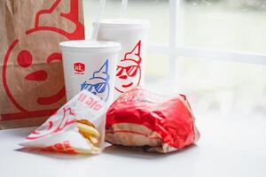 WASHINGTON, USA - August 08, 2024 - A classic fast food spread from Jack in the Box two cups of soda, a bag of fries and a wrapped burger. The cups feature the chain's iconic mascot with sunglasses. photo