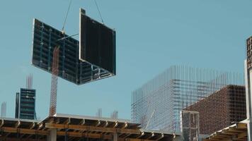 Large construction panel lifted by crane on building site. A large construction panel being lifted by a crane at a building site, with visible scaffolding and rebar in the background. video