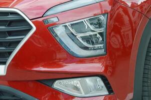A fragment of the body of a modern red passenger car - the front headlight and part of the hood. photo