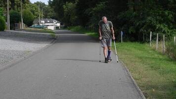 man with broken leg walks down the street,his left leg is in cast adapted for walking in special shoes,he moves with crutches,which reduces the load on the broken foot,concept of rehabilitation video