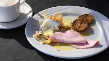 Plate with breakfast on table illuminated by morning sun, eggs, ham and zucchini slices next to cup of coffee in restaurant, Hearty breakfast concept, video