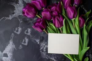 mockup white blank paper card with purple tulips flowers top view on black concrete background, floral template empty card flat lay for design photo