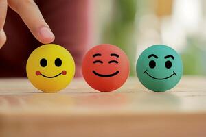 The finger of the hand points to three multi-colored balls with different smiles and emotions photo