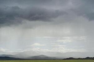 Rays of light shine down from a cloudy sky into a fields. Sun beams bursting through raining clouds over a fields. mountains against the background of rain in the distance. Background for text photo