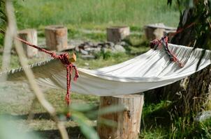 The edge of a hammock among the greenery. The white fabric of the hammock is suspended in the greenery of the garden. Fragment of a hammock for relaxation in a green garden photo