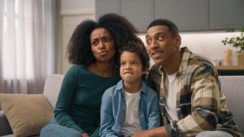 Excited happy playful African American ethnic family mother father embracing little boy child playing game parents kid watching funny TV show movie posing making faces grimacing indoors home apartment photo