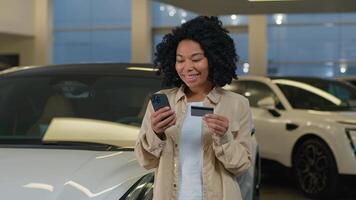 africano americano contento cliente mujer comprador sostener crédito tarjeta móvil teléfono compras comprando nuevo lujo eléctrico automóvil en concesión auto salón compra vehículo crédito pago coche compartiendo Servicio foto