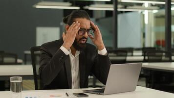 Upset worried shocked frustrated Indian businessman read terrible information problem trouble error unsaved report on laptop computer in office lost failure sad business man stressed reading bad news photo