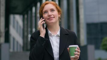 cerca arriba contento sonriente elegante rojo peludo caucásico mujer hembra niña mujer de negocios estudiante traje hablar hablando móvil teléfono teléfono inteligente llamada amigos haciendo en línea orden bebida café fuera de ciudad calle foto
