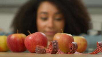 Happy health smiling African American woman ethnic girl female at home kitchen looking enjoying fruits apples glass of water measuring tape at table weight control diet healthy nutrition dieting slim photo