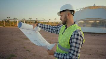 Pensive thoughtful professional Caucasian male man guy uniform engineer worker analysing reading project blueprint structure build plan confused inspector architect looking around farmland field park photo