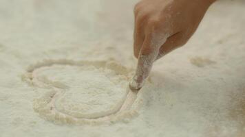 Close up cropped view African American little girl child hand finger drawing heart on flour cooking at table home kitchen unrecognizable kid daughter draw love shape on powder wheat dust cook family photo