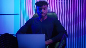 Hacker programmer computer worker gamer African American man in headphones male guy typing laptop online data internet security gaming play game innovation futurism sitting at chair cyber crime photo