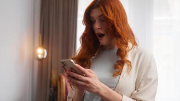 Satisfied Caucasian woman shocked girl type screen mobile phone device happy lady saying wow surprise gladness emotion pleased excited ginger female smiling success good news excellent result at home photo