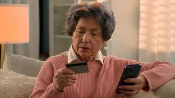 caucásico antiguo mujer mayor retirado abuelita mayor hembra abuela comprador cliente compras en línea Internet pago con móvil teléfono y banco crédito tarjeta celebrar contento con comprando teléfono inteligente a hogar foto