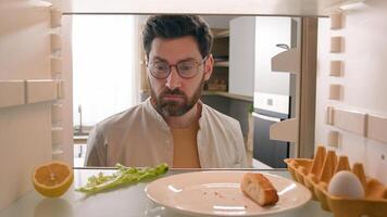 Man hungry guy open empty refrigerator with half lemon, nasty lettuce leaf, one egg, slice of bread order food delivery buying products with mobile phone deliver app point of view from inside fridge photo