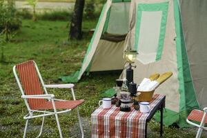 selective focus of Vintage drip coffee set and baguette on a table in front of a camping tent in the forest in the morning, soft focus. photo