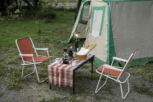 selective focus of Vintage drip coffee set and baguette on a table in front of a camping tent in the forest in the morning, soft focus. photo