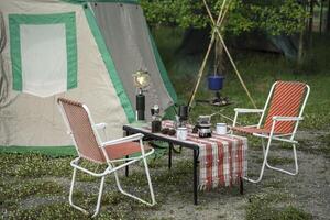 The vintage drip coffee set and baguette are in selective focus on a table in front of a camping tent in the forest in the morning. photo