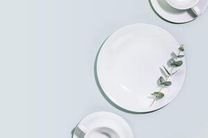Empty dishes and cups with eucalyptus twig on blue background with copy space photo
