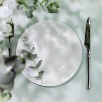 Empty white plate with fork and knife on blue background with eucalyptus leaves photo