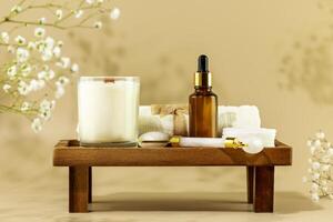 Serum, face roller, towel and candle on wooden podium on beige background photo
