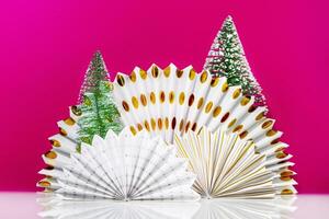 White table with paper fans and new year trees on magenta background photo