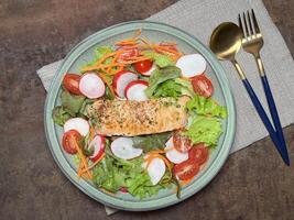 A perfectly cooked salmon fillet with a herb crust, served on a bed of fresh greens with cherry tomatoes and radishes with golden spoon on rustic table photo