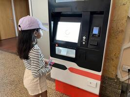 Asian little girl in front of the ticket machine printing tickets photo