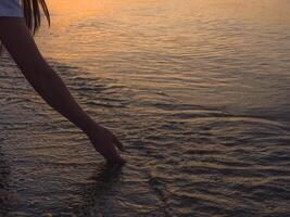 As the sun sets, a woman's hand reaches out to touch the water her hand delicately brushing the surface, capturing the tranquility of the moment as ripples form and fade in the warm glow of dusk. photo