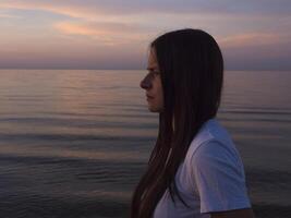 A young woman enjoys the view as the sunset unfolds on the seashore, with the golden rays of the sunset reflecting off the water, creating a mesmerizing and calming atmosphere. photo