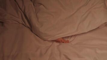 restless feet of a kid boy on a sheet under a blanket at night. Baby child girl with bare legs tosses and does not fall asleep in bed in the bedroom in evening video