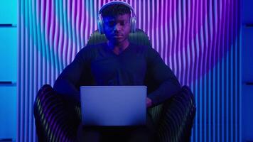 Hacker programmer computer worker gamer African American man in headphones male guy typing laptop online data internet security gaming play game innovation futurism sitting at chair cyber crime video
